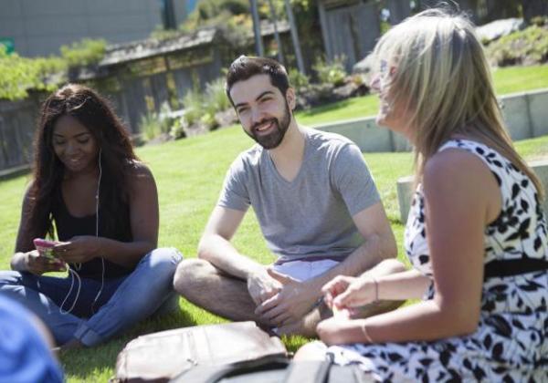 One male and two female students sitting together on the grass on campus