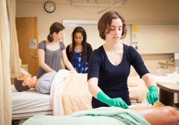 Young women tending to practice dummies in a mock hospital ward