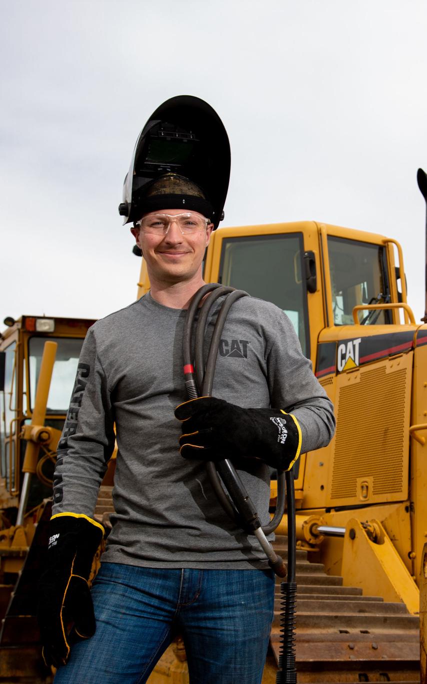 A young man in welding gear in front of industrial equipment