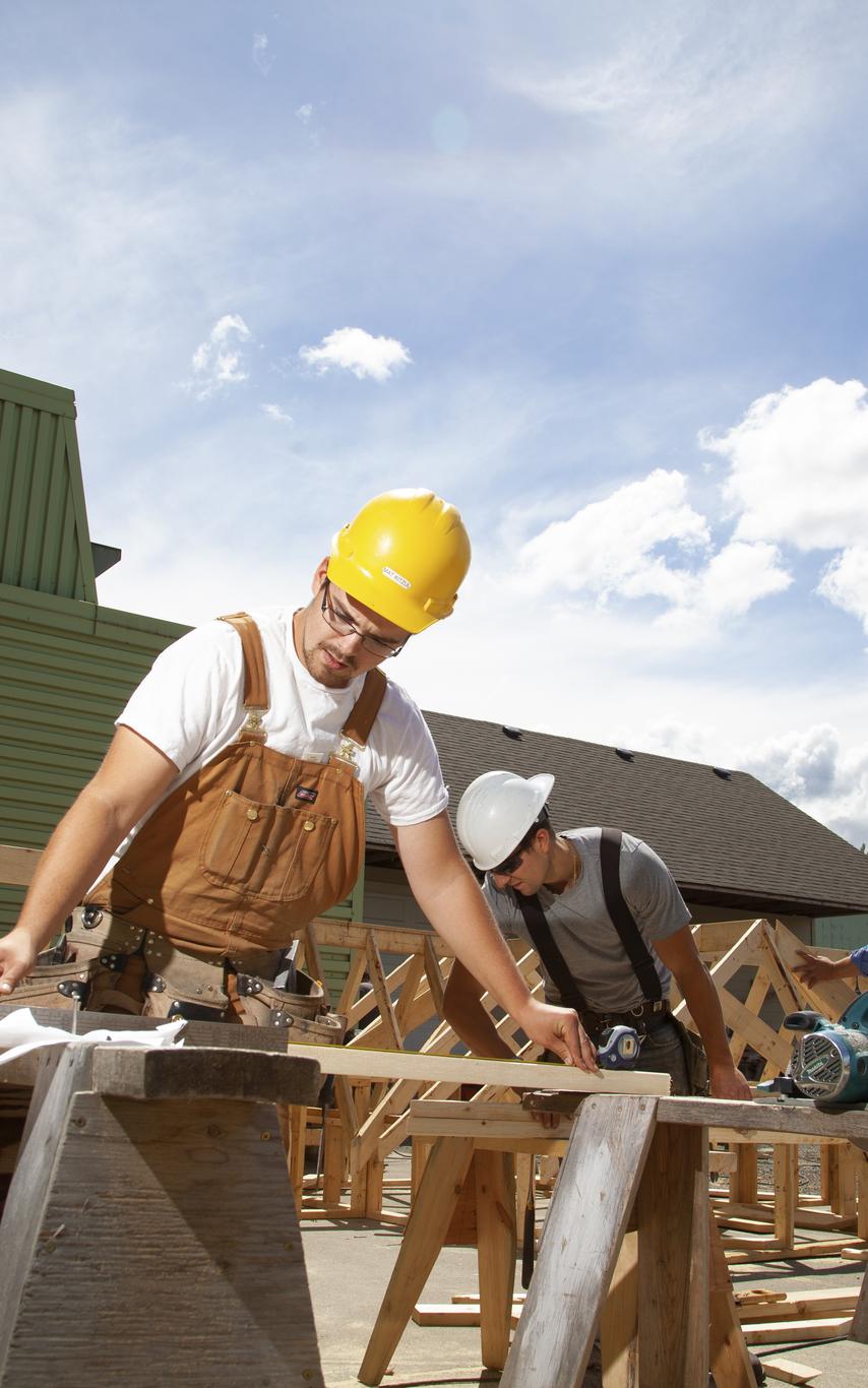 Three men doing carpentry work outside under a blue sky