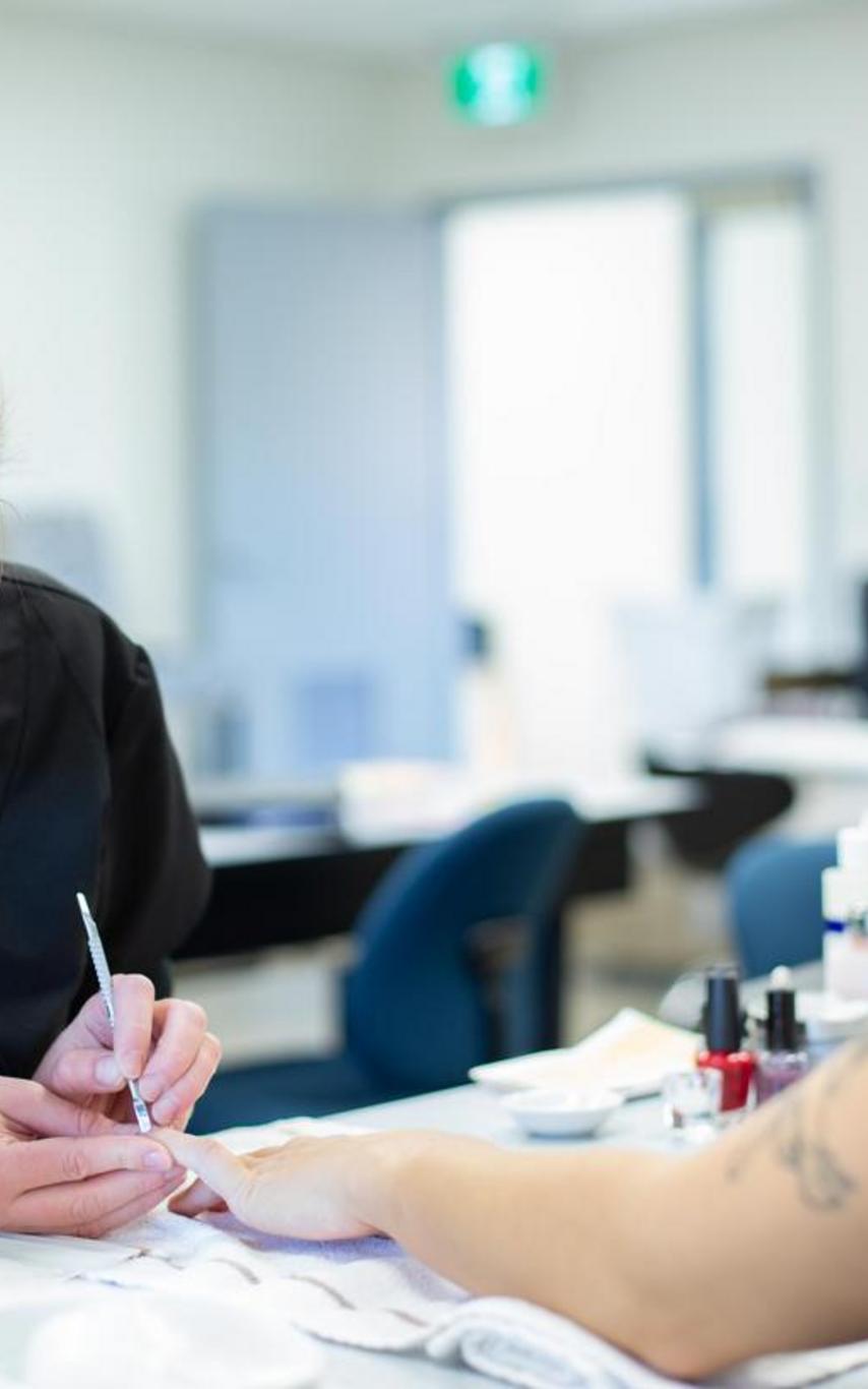 A blond-haired woman working on a dark-haired woman's fingernails