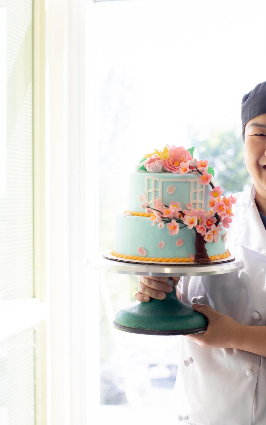 Female student in chef's whites presenting a cake on a platter